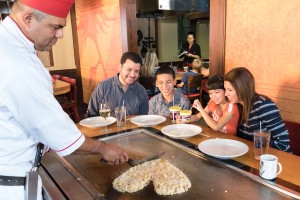 a group of people sitting at a table with plates and a chef cutting food